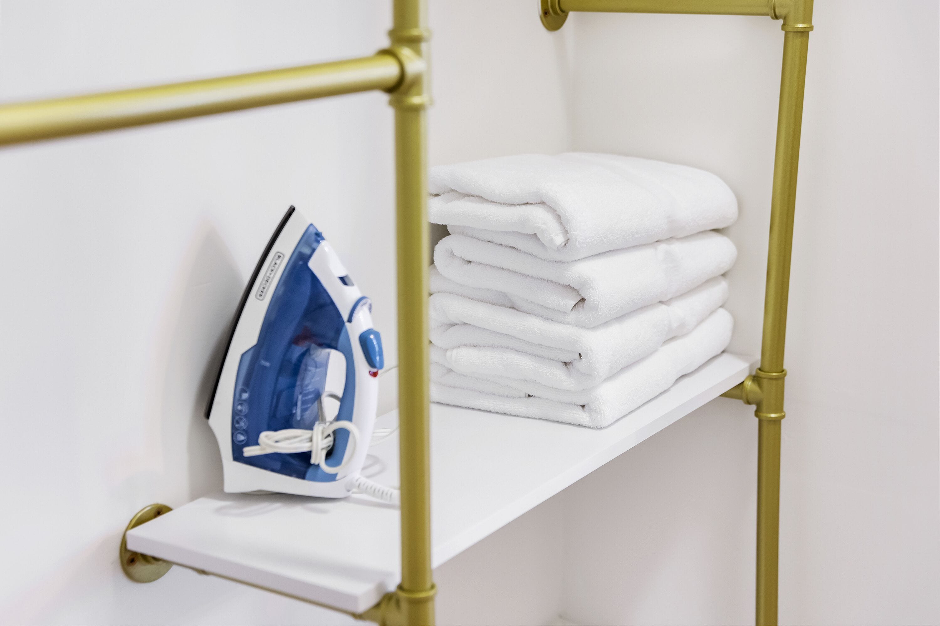 A white shelf with neatly stacked white towels and a blue and white iron.