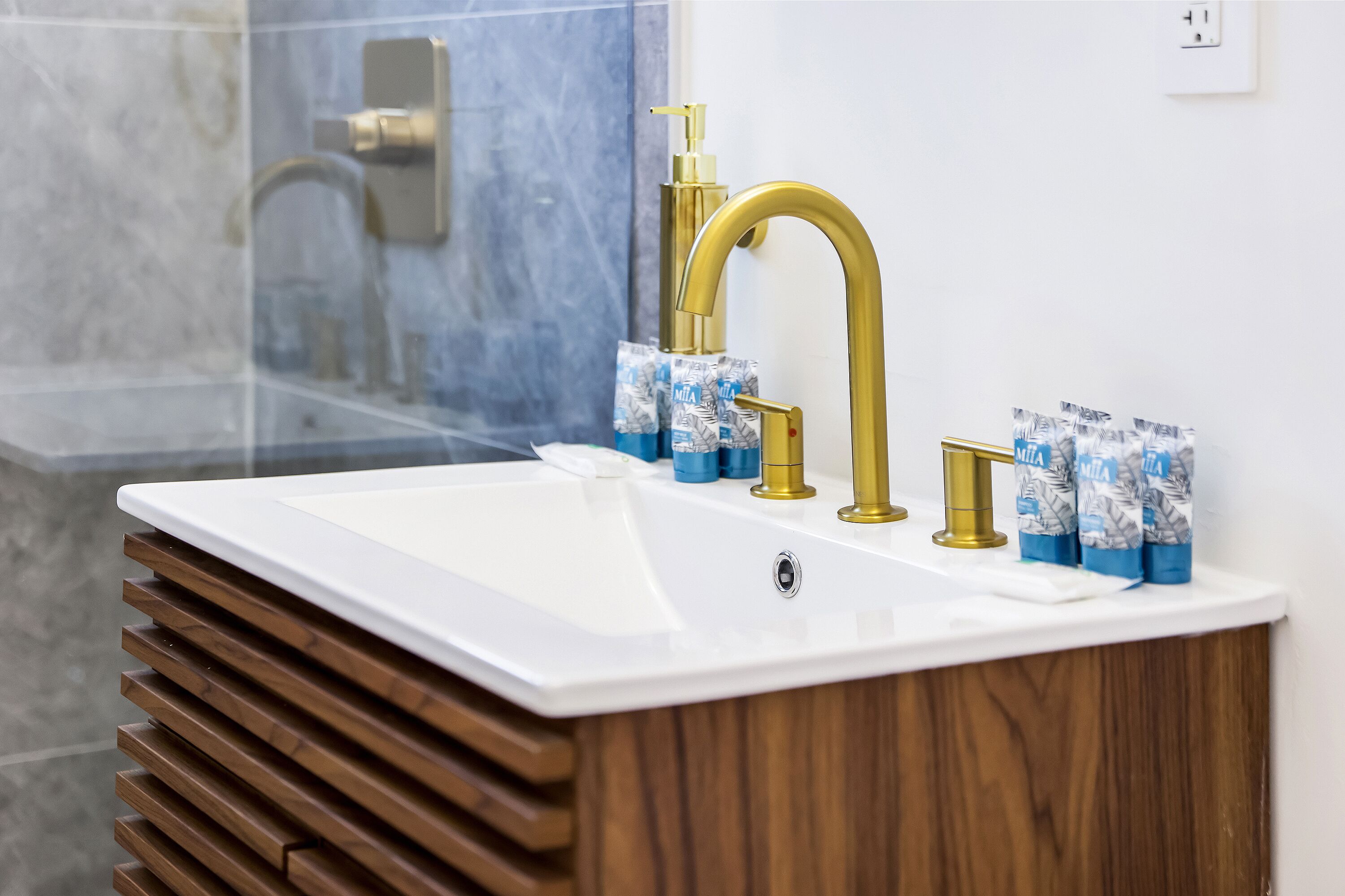 A bathroom with a white sink, gold faucets, and wooden slats.