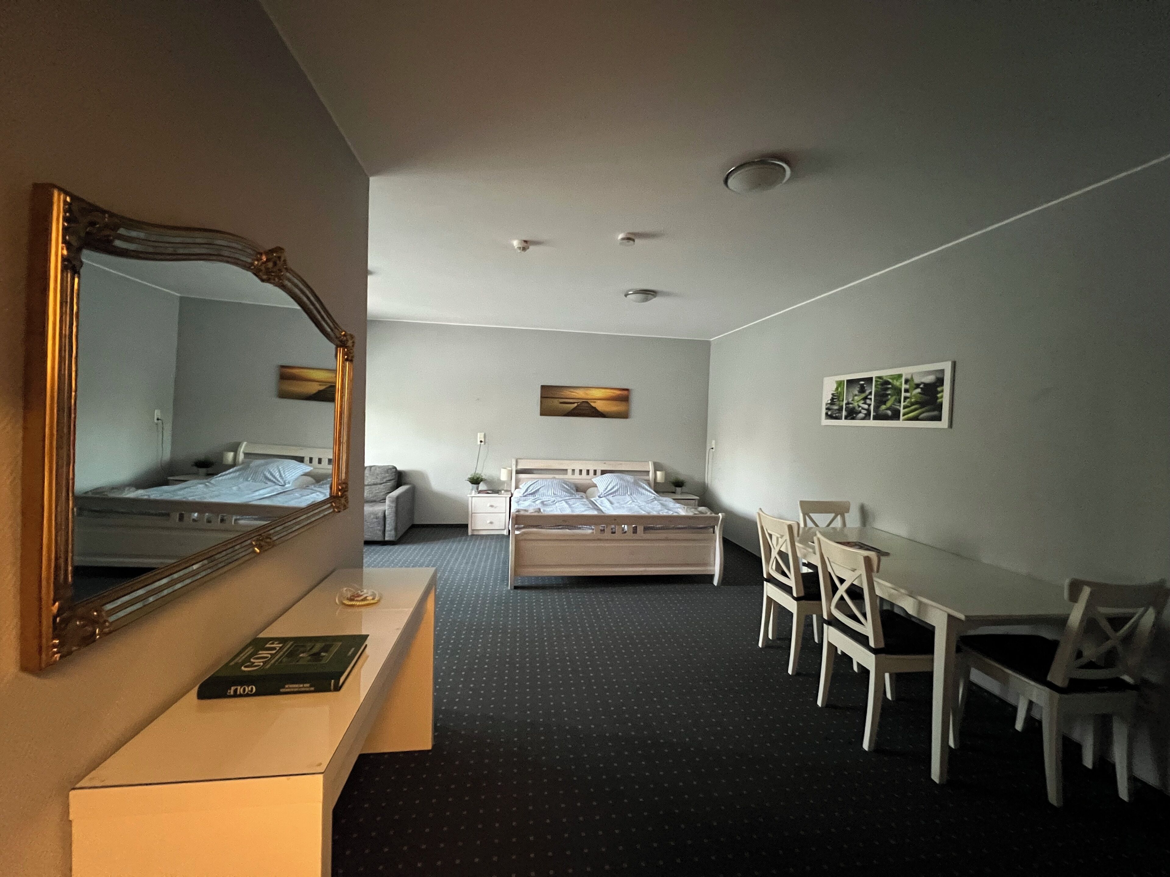 Ein Hotelzimmer mit Bett, Schreibtisch, Stuhl, Kommode, Spiegel und kleinem Tisch.