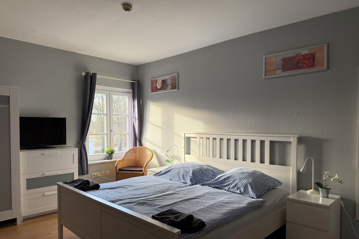 A bedroom with a bed, bedside tables, a TV, a chair, and a window with curtains.