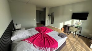 Ein modernes Hotelzimmer mit einem großen Bett, einem Schreibtisch mit einem Flachbildfernseher und einem begehbaren Kleiderschrank.