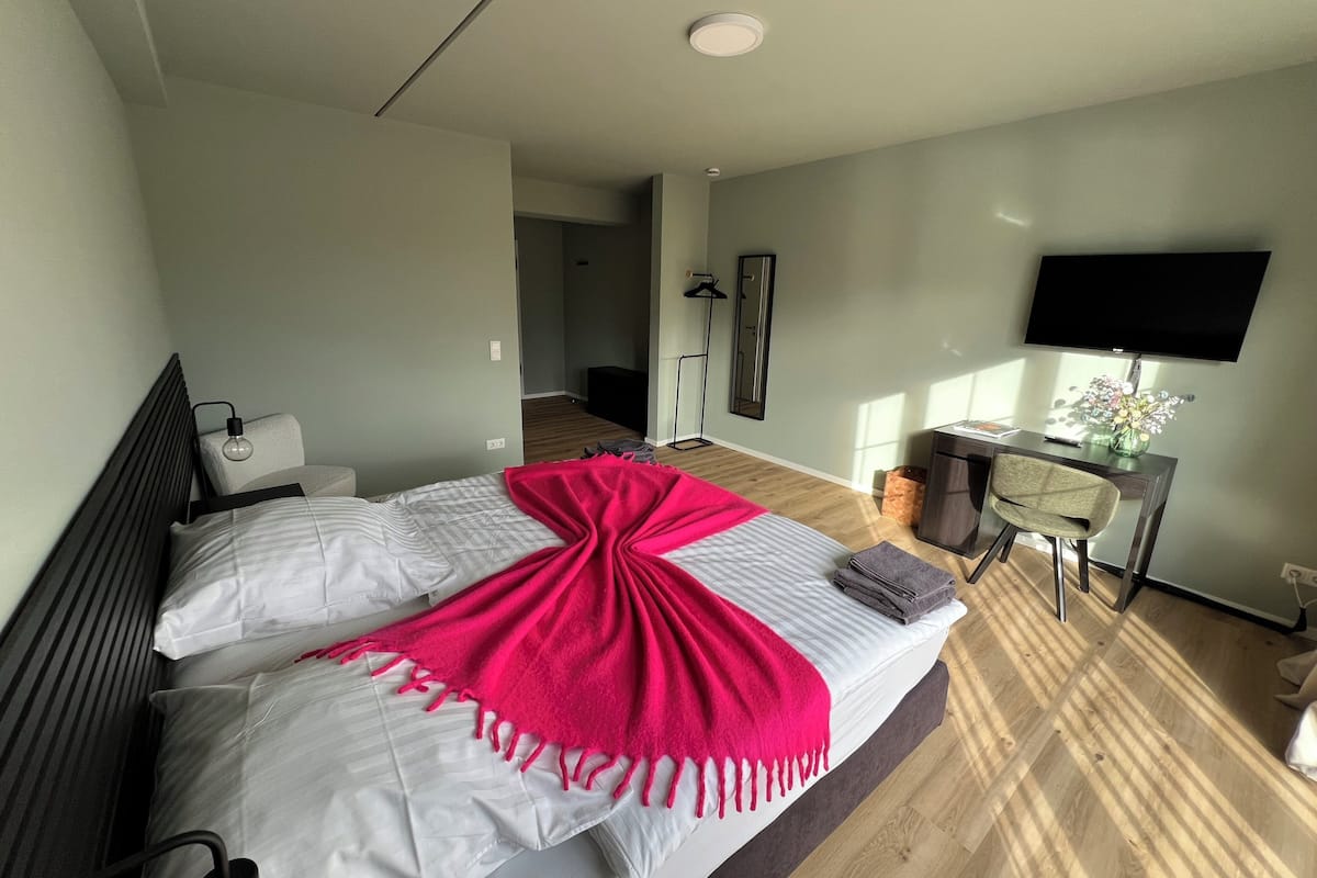 A modern hotel room with a large bed, a desk with a flat-screen TV, and a walk-in closet.