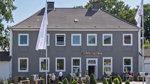 Ein zweistöckiges Gebäude mit grauer Fassade und weißem Zierrat, mit einem Schild, auf dem 