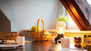 Ein Frühstücksambiente mit einem Korbfruchtregal, einer Kerze und einem Marmeladenglas auf einem Holztisch.