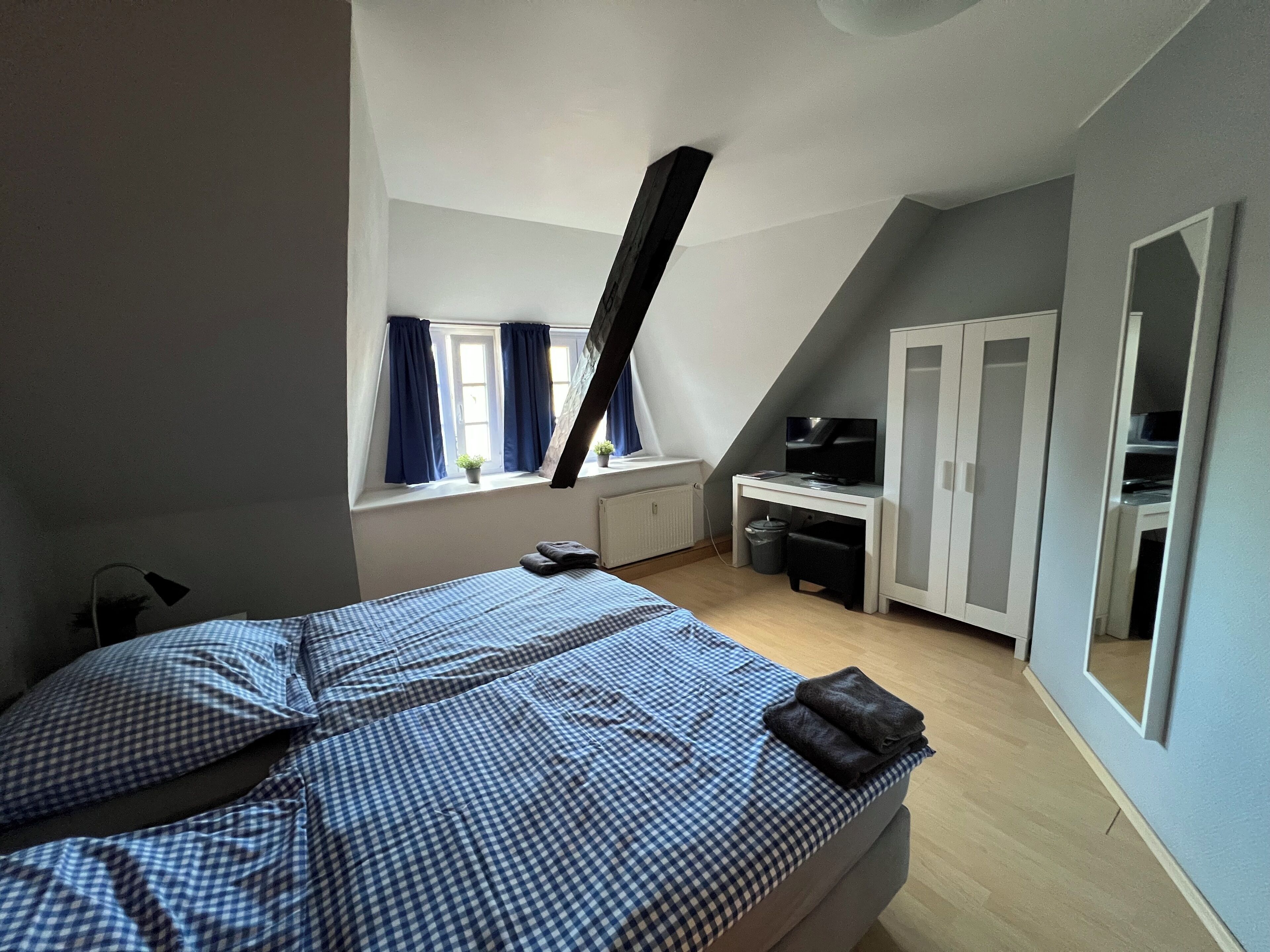 Ein Schlafzimmer mit Bett, Schreibtisch, Kleiderschrank und einem Fenster mit Vorhängen.