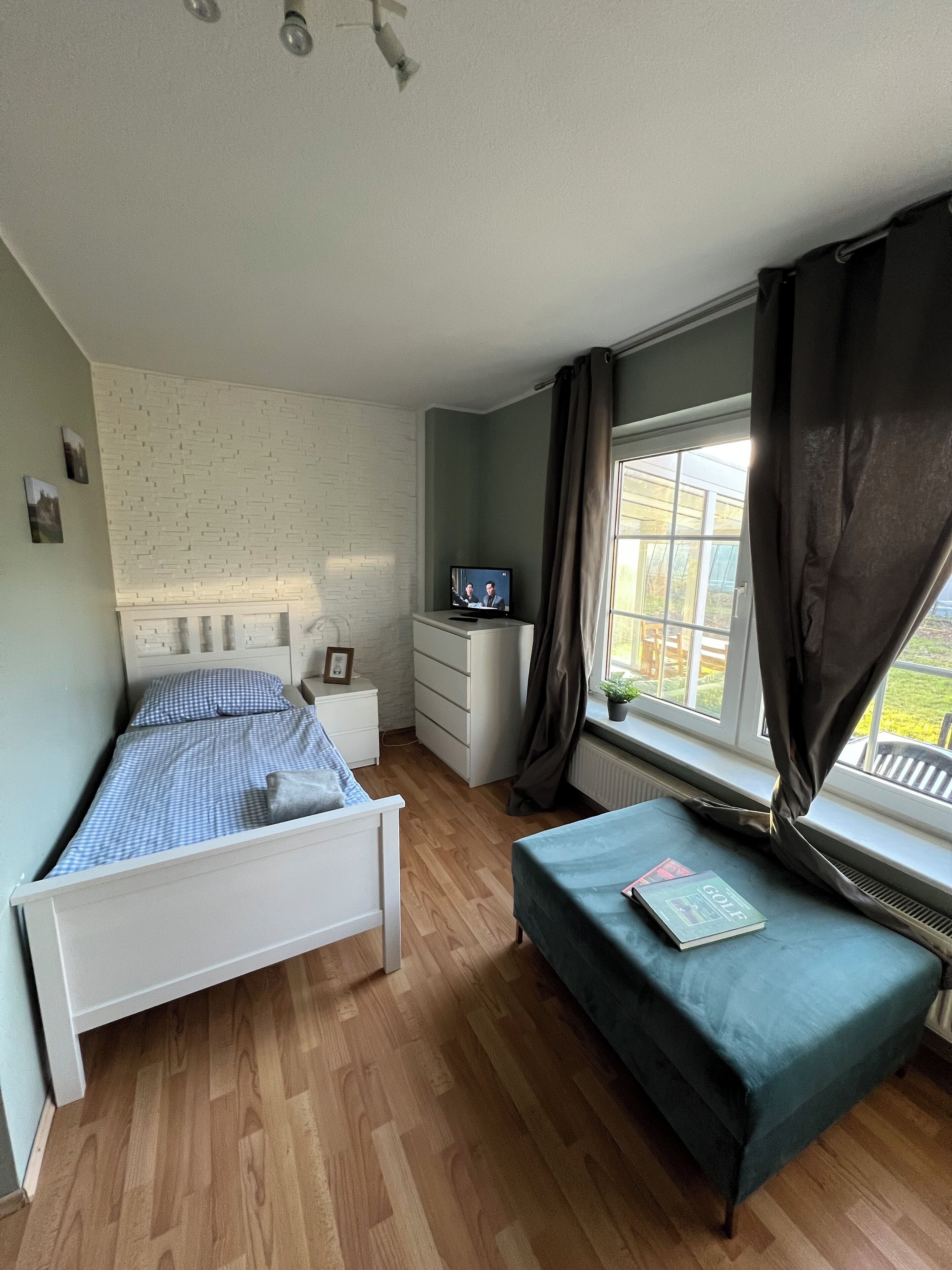 A bedroom with a bed, a bench, a TV, and a window with curtains.