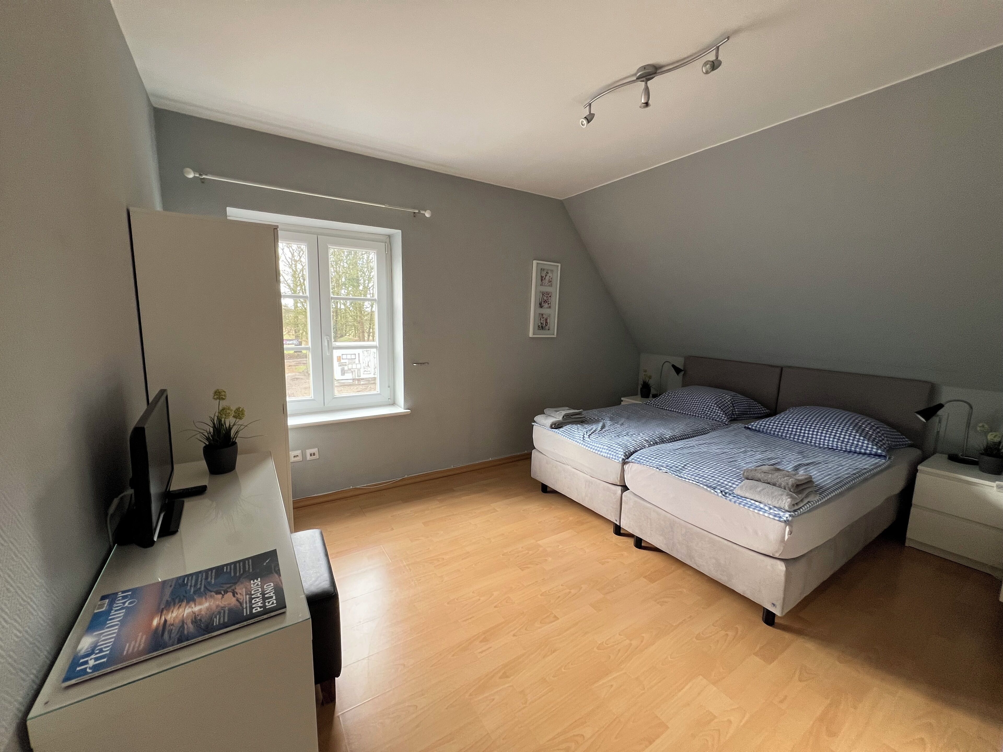 Ein Schlafzimmer mit Bett, Schreibtisch, Stuhl, Fenster und Deckenleuchte.