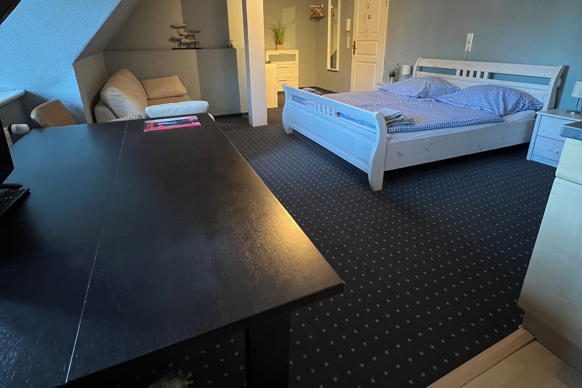 A bedroom with a bed, a desk, a chair, and a small table.