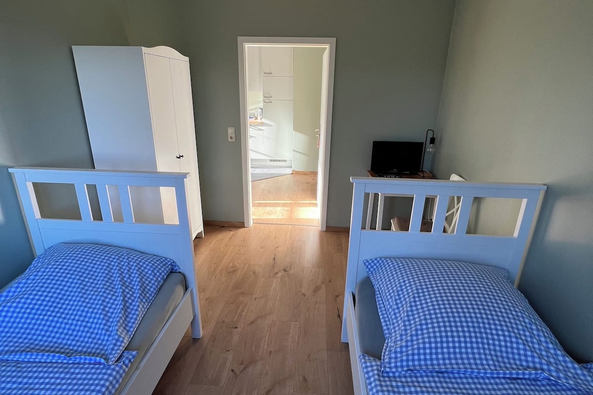A room with two single beds, a wardrobe, a desk, and a door leading to another room.