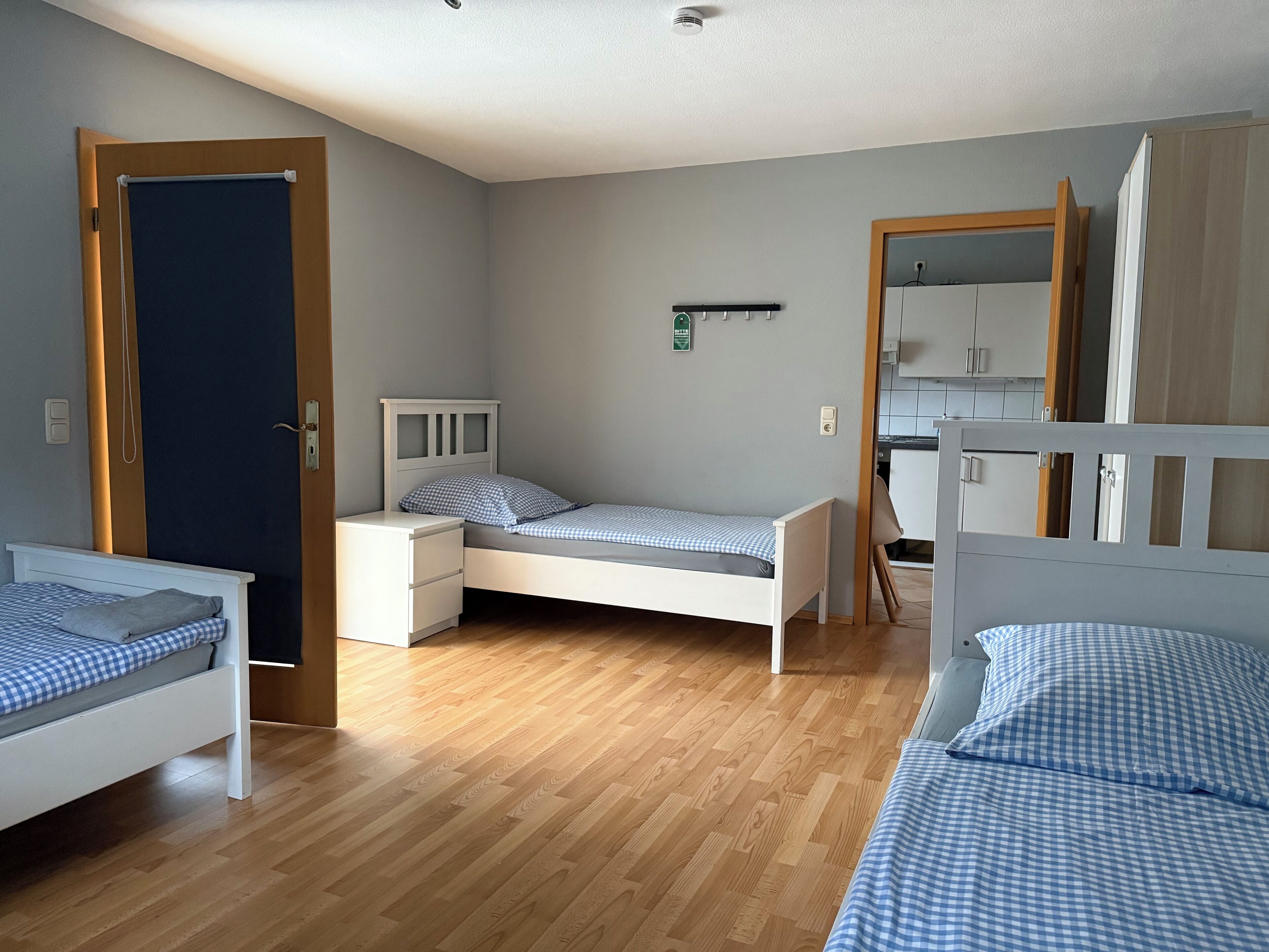 Une chambre avec deux lits simples, une petite table de chevet, une armoire et une porte donnant sur un coin cuisine.