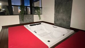 A modern spa room with a large hot tub, red cushioned seating, a glass ceiling, and a view of the cityscape at night. - Holiday & Business Hotel - Ao lado do Centro de Eventos e Arena Conda (Chapecó)