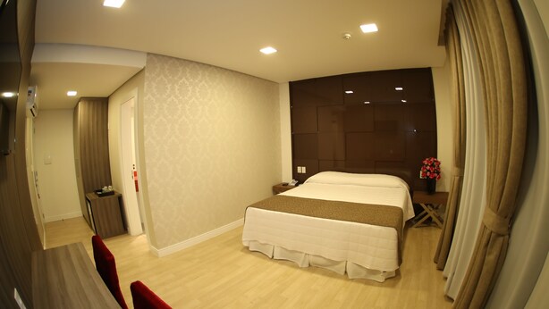 A modern hotel room with a large bed, a bedside table, a nightstand, and a small desk. - Holiday & Business Hotel - Ao lado do Centro de Eventos e Arena Conda (Chapecó)