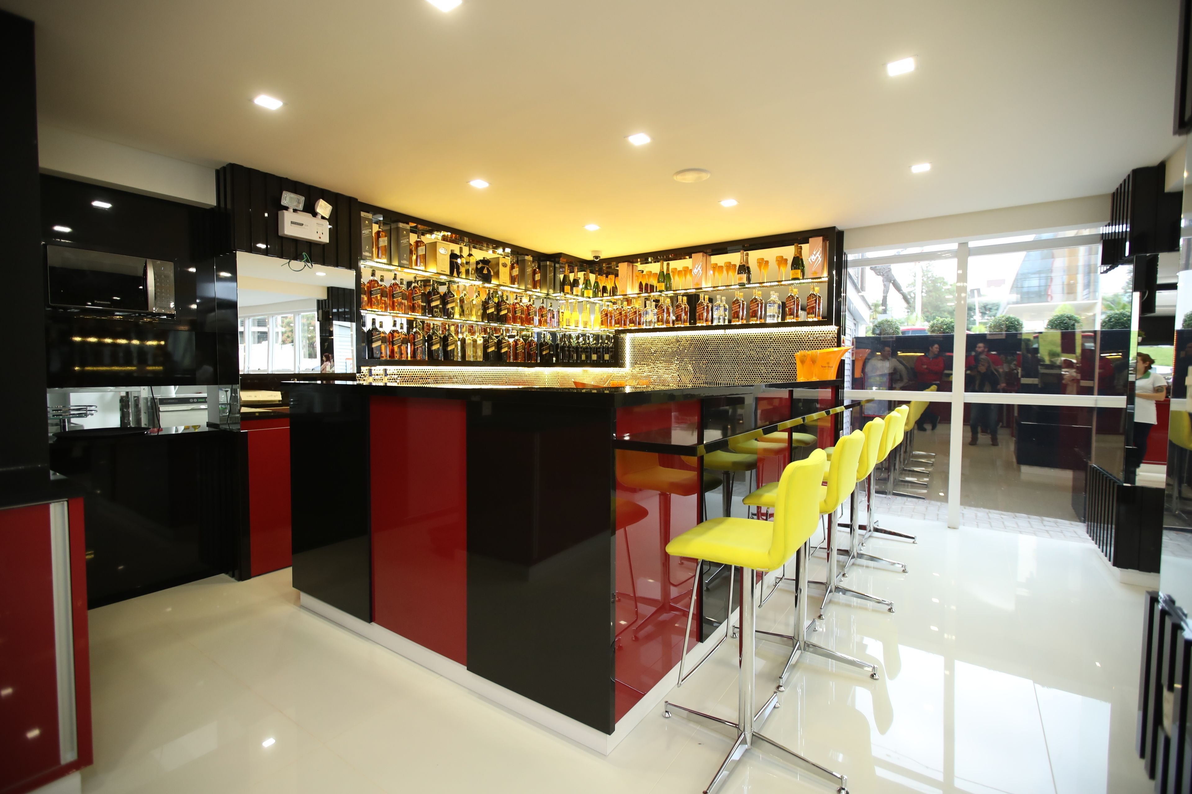 A modern bar area with a black and red color scheme, a glass partition, and yellow bar stools.