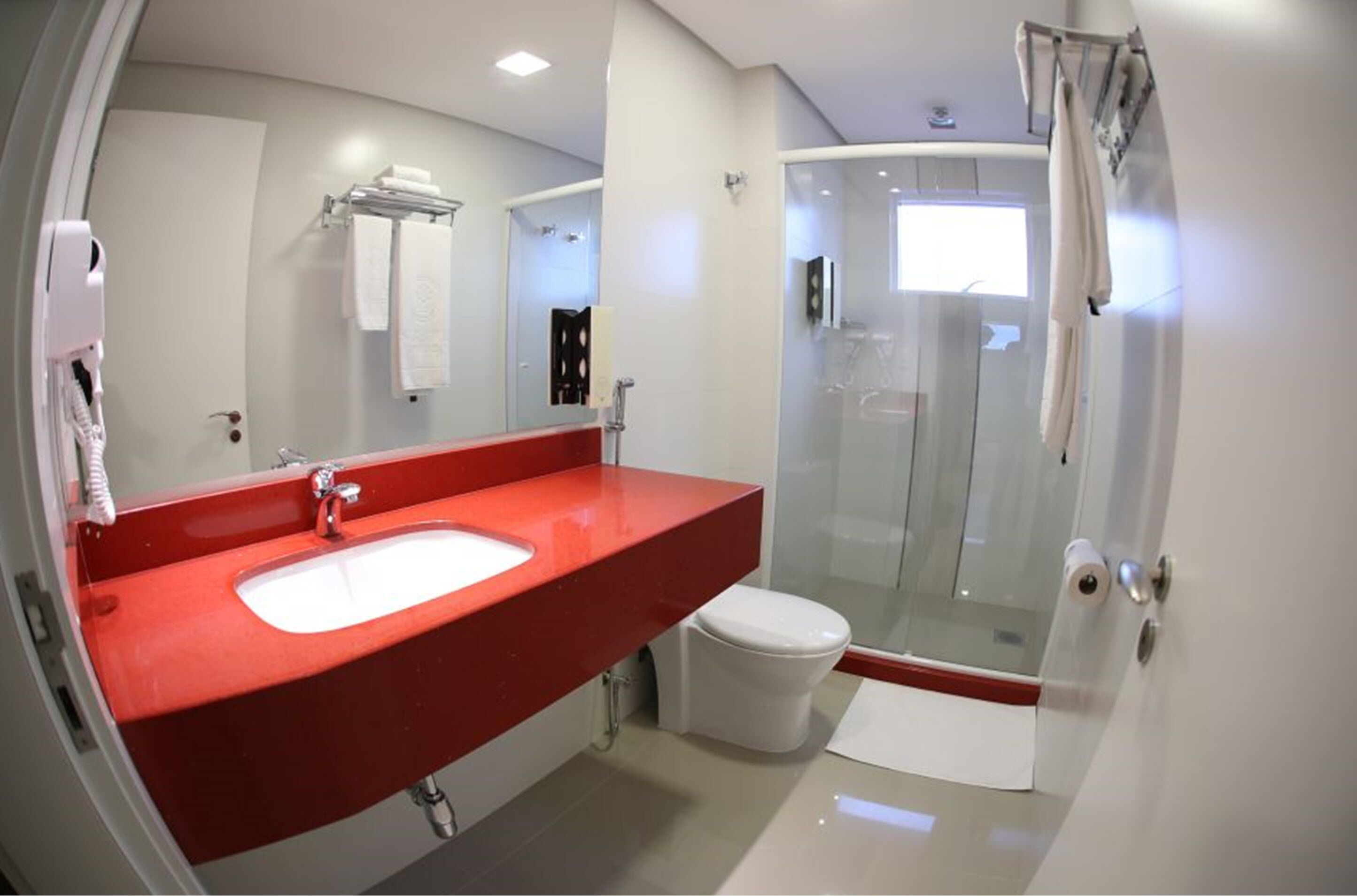 Un baño moderno con lavamanos rojo, inodoro blanco y cabina de ducha con paredes de vidrio.