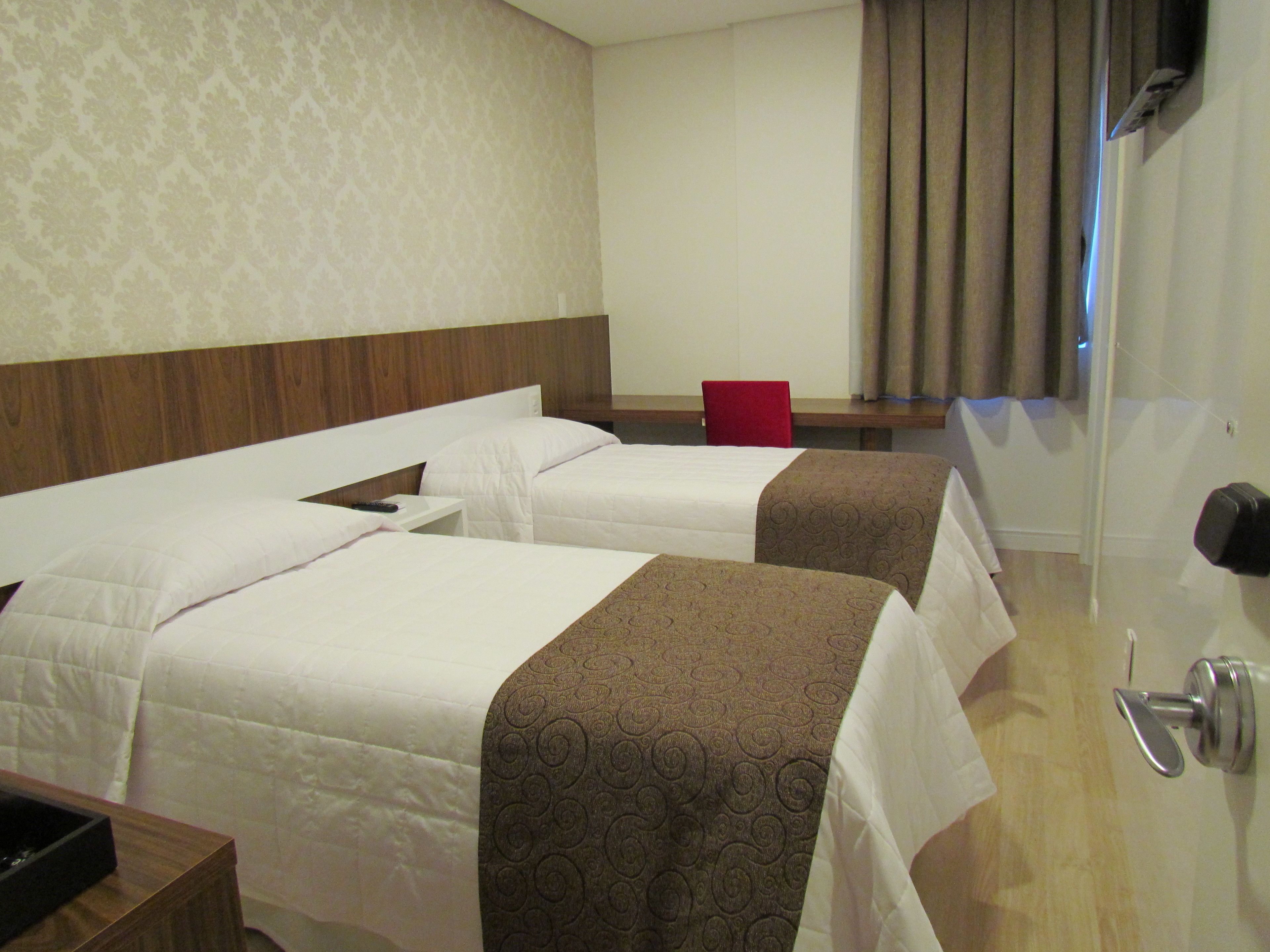 A hotel room with two beds, a desk, a chair, and a bathroom door.