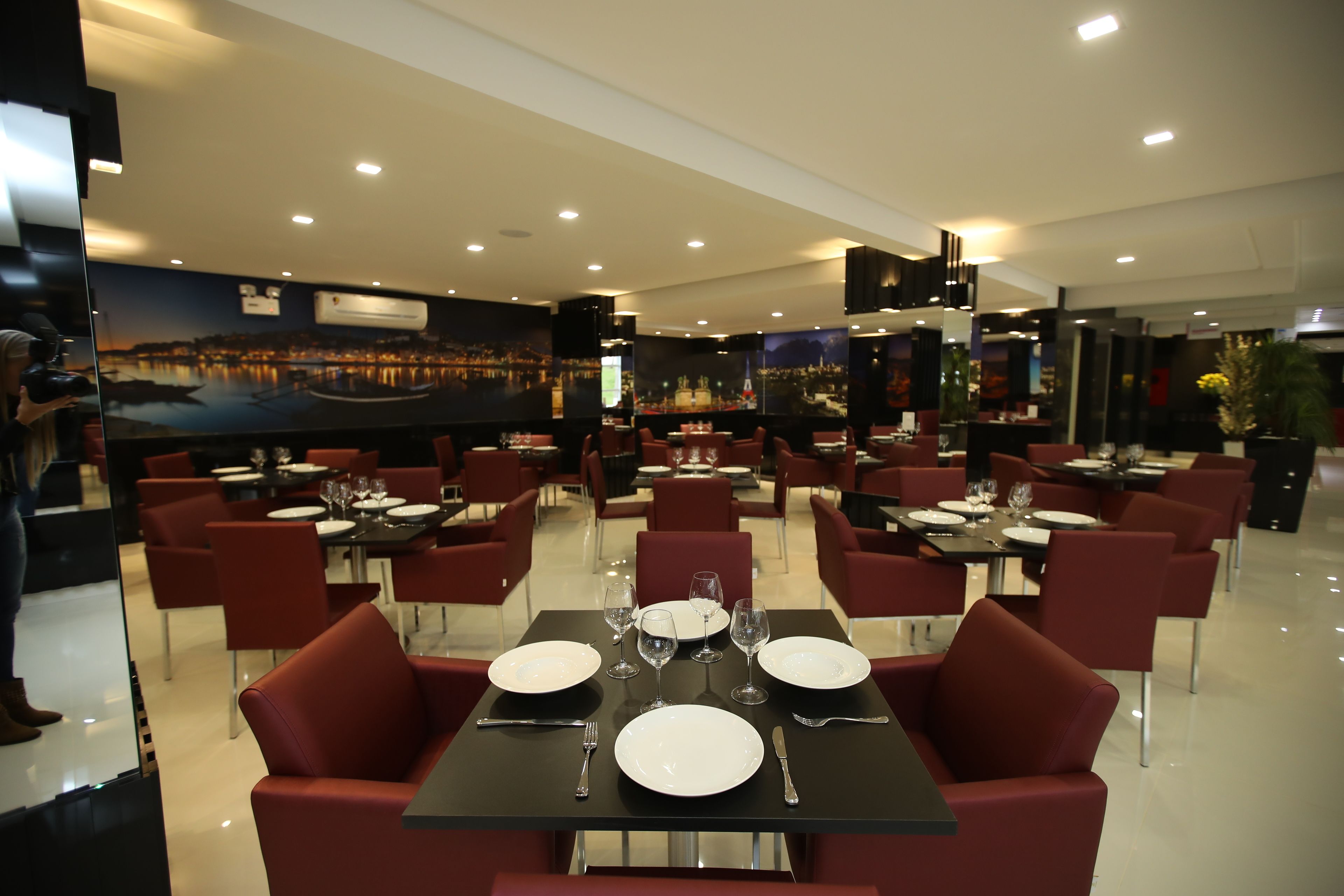 Un restaurante con mesas dispuestas para comer, sillas rojas y un mural de paisaje urbano en la pared.