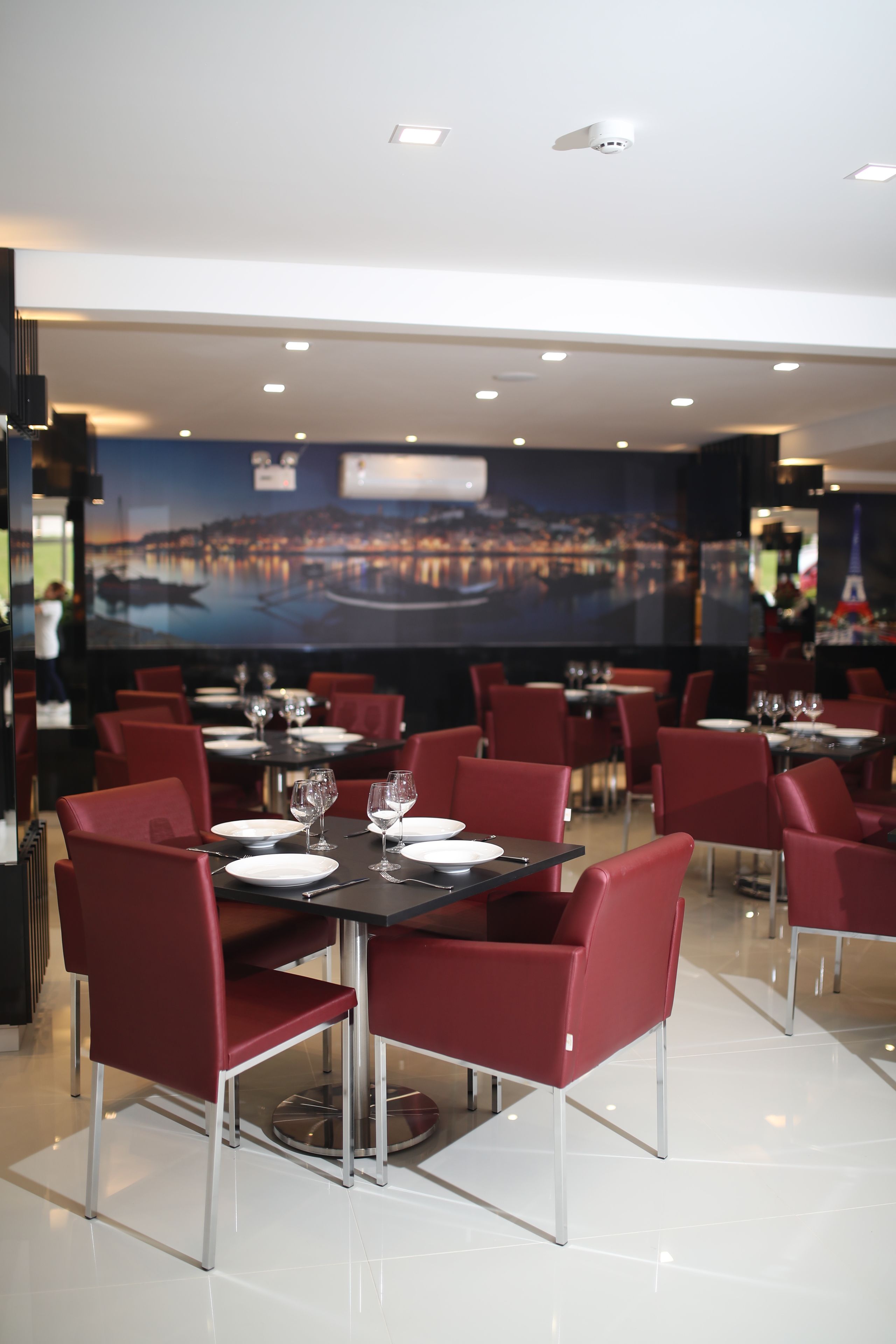 A restaurant with tables set for dining, red chairs, and a cityscape mural on the wall.