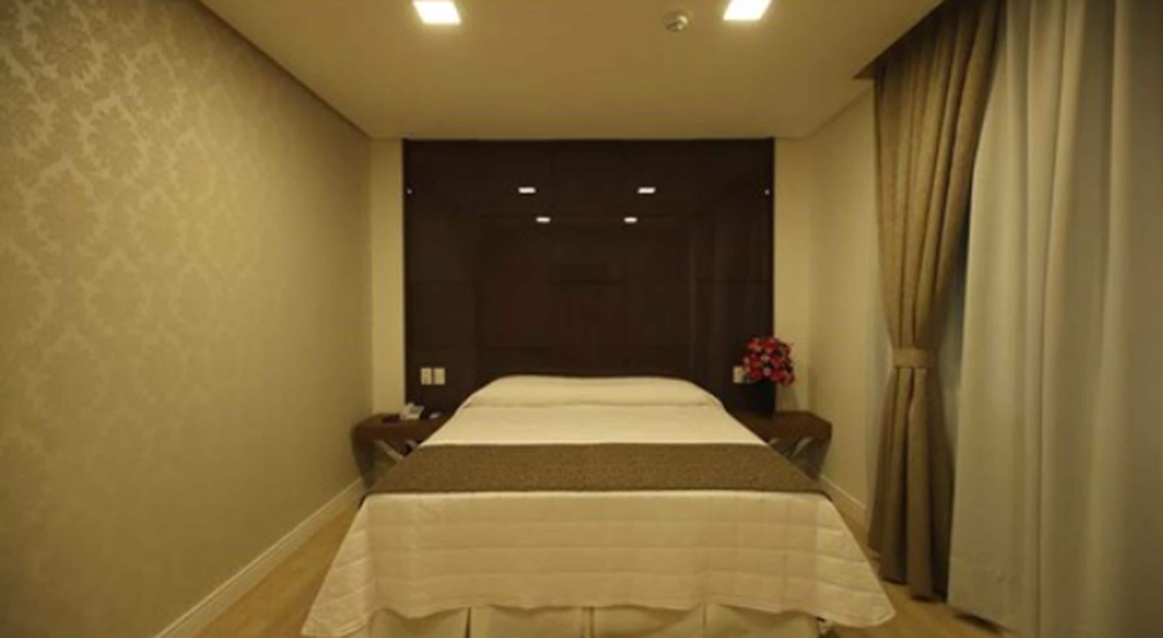 A hotel room with a large bed, a nightstand, a vase with flowers, and a curtain.