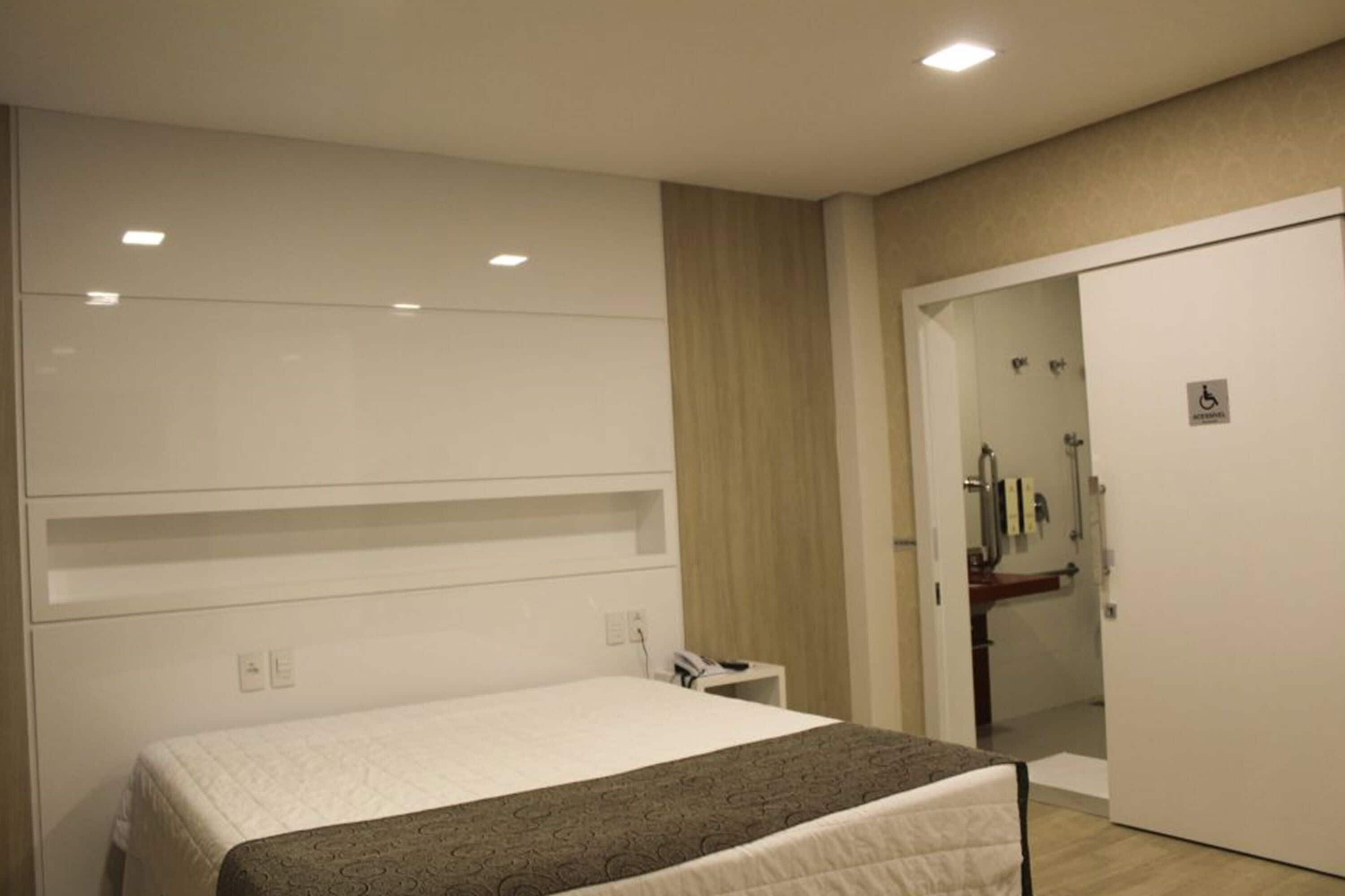 Une chambre d’hôtel avec un lit, une armoire, une petite table de chevet et une salle de bain visible à travers une porte ouverte.