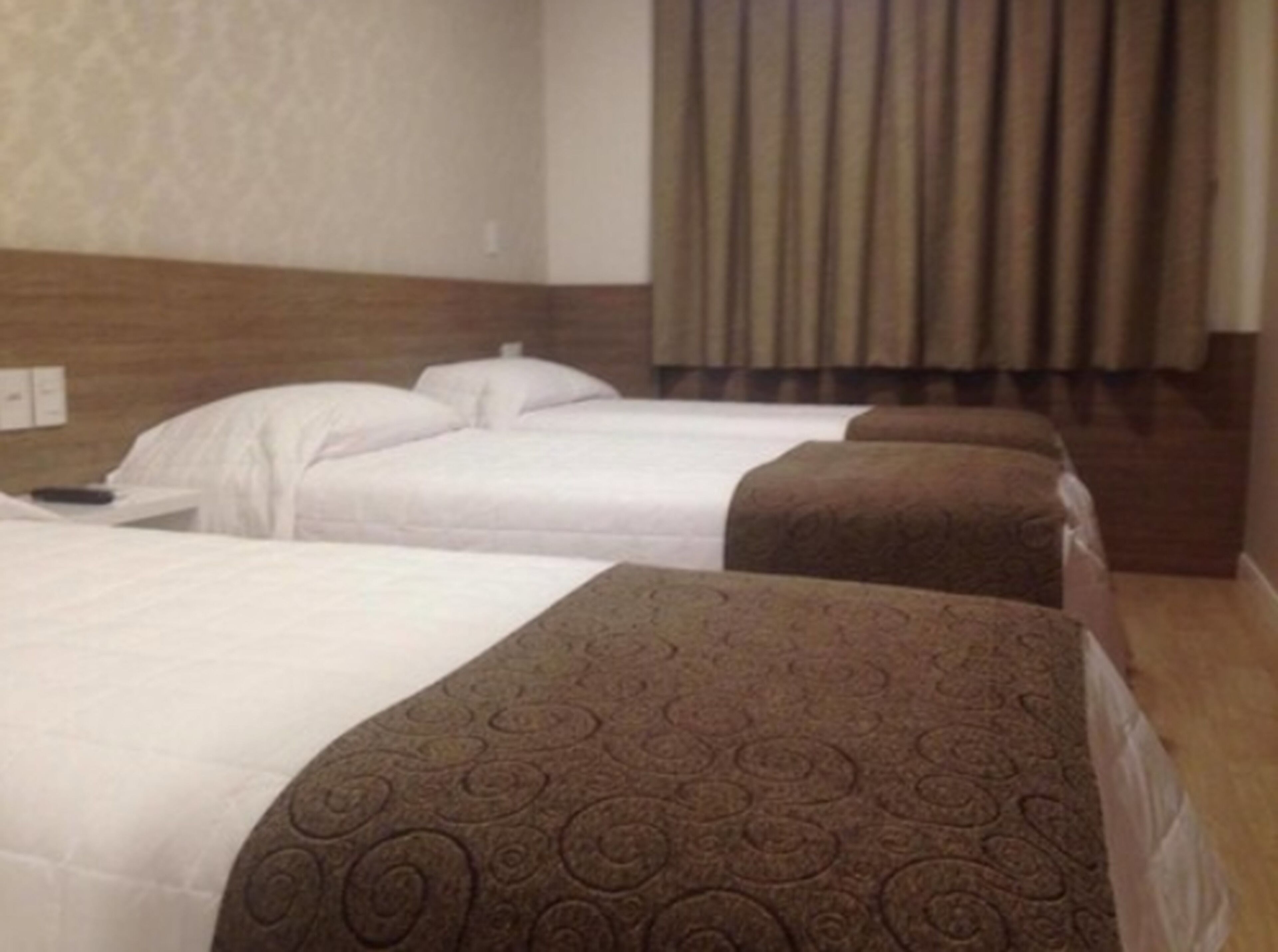 A hotel room with three beds, each with a patterned bedspread.