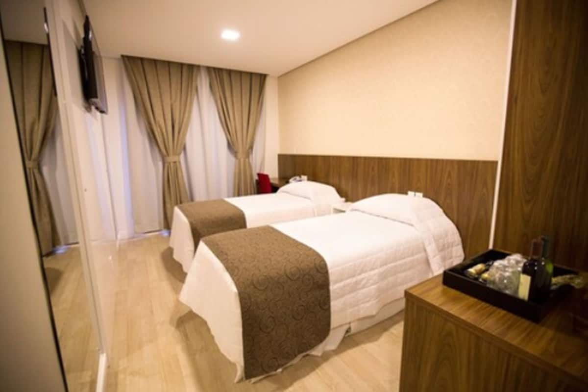 Ein Hotelzimmer mit zwei Betten, einem Holz-Kopfteil, einem kleinen Nachttisch mit Tablett und einem an der Wand montierten Fernseher.