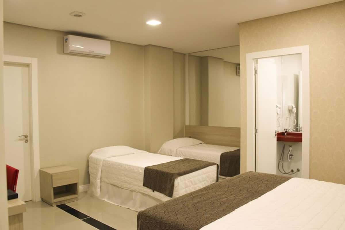 Ein Hotelzimmer mit zwei Einzelbetten, einem kleinen Nachttisch, einem Spiegel und einem Badezimmer mit Waschbecken und Dusche.