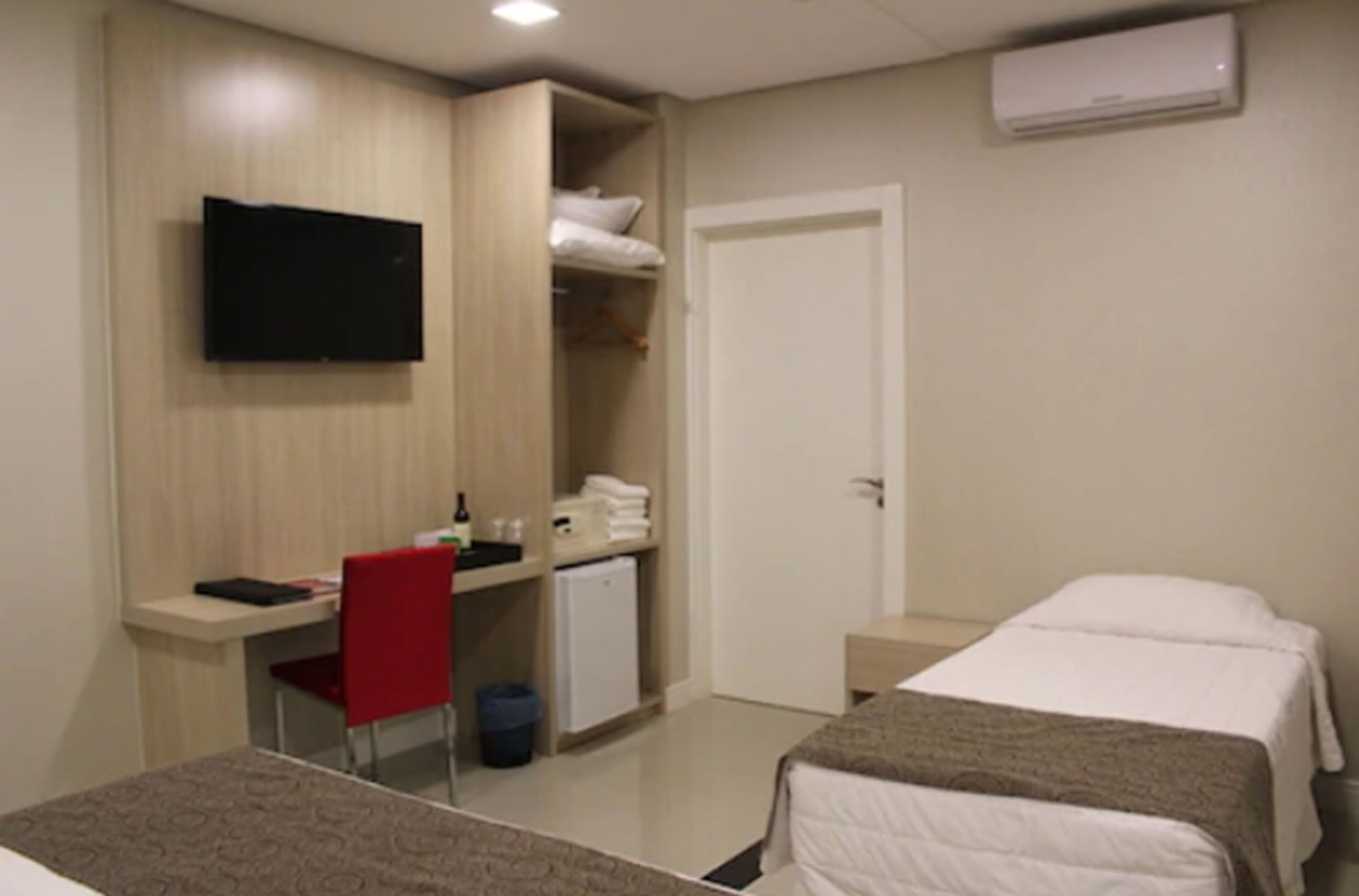 Una habitación de hotel con cama, escritorio, silla, televisor y armario.