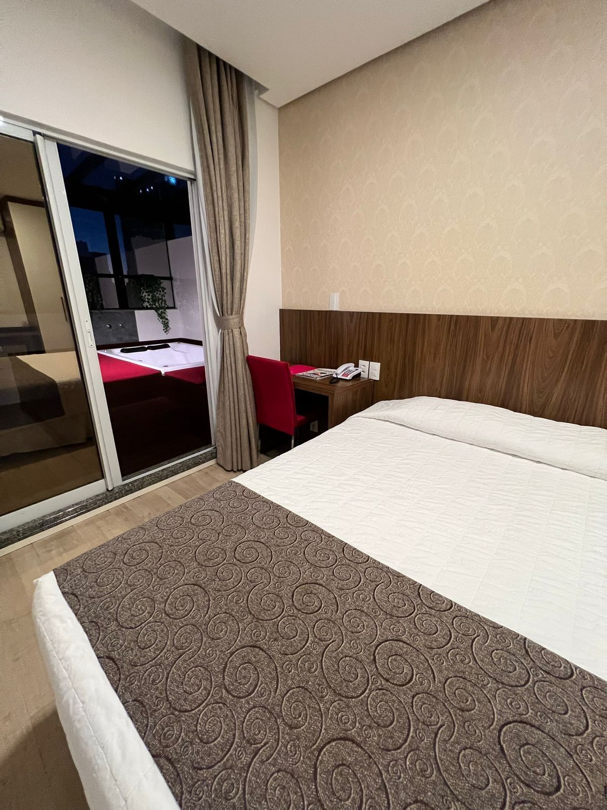 A hotel room with a bed, a desk with a telephone, and a view of the outside.