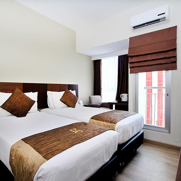 A hotel room with two beds, a desk, a chair, an air conditioning unit, and a window with curtains.