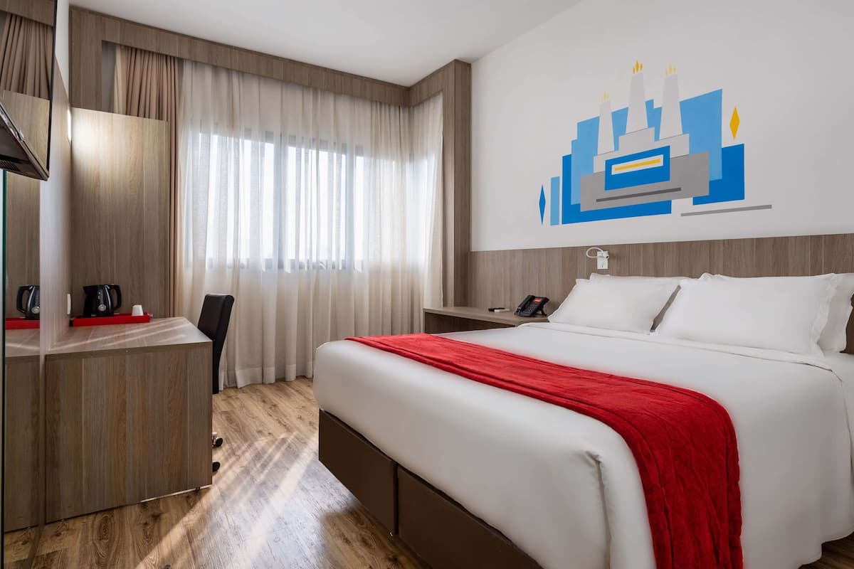 Habitación de hotel con cama, escritorio, silla, cafetera y teléfono montado en la pared.