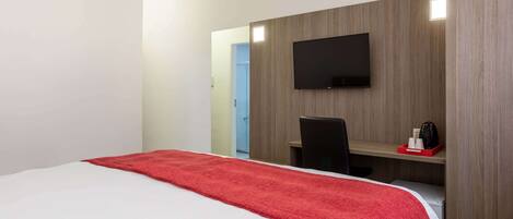 Habitación de hotel con cama, escritorio, silla, televisor y pequeña kitchenette.