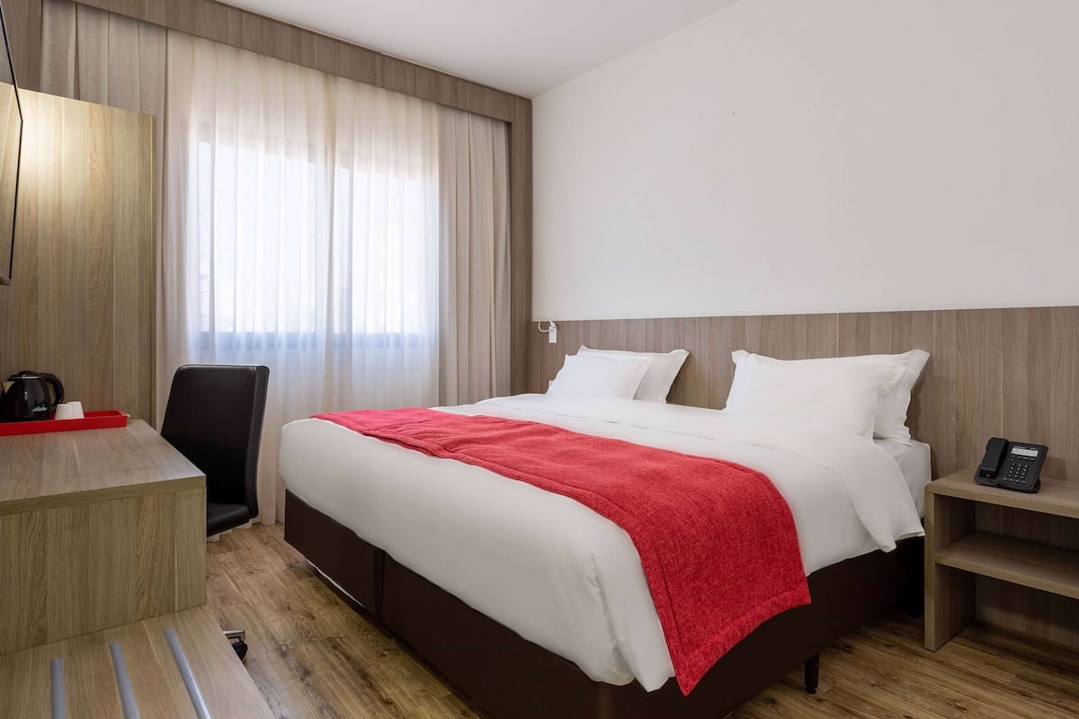 Habitación de hotel con cama, escritorio, silla, mesita de noche con teléfono y ventana con cortinas.