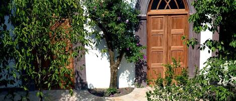 A courtyard with a brick pathway, a wooden door, and lush greenery.
