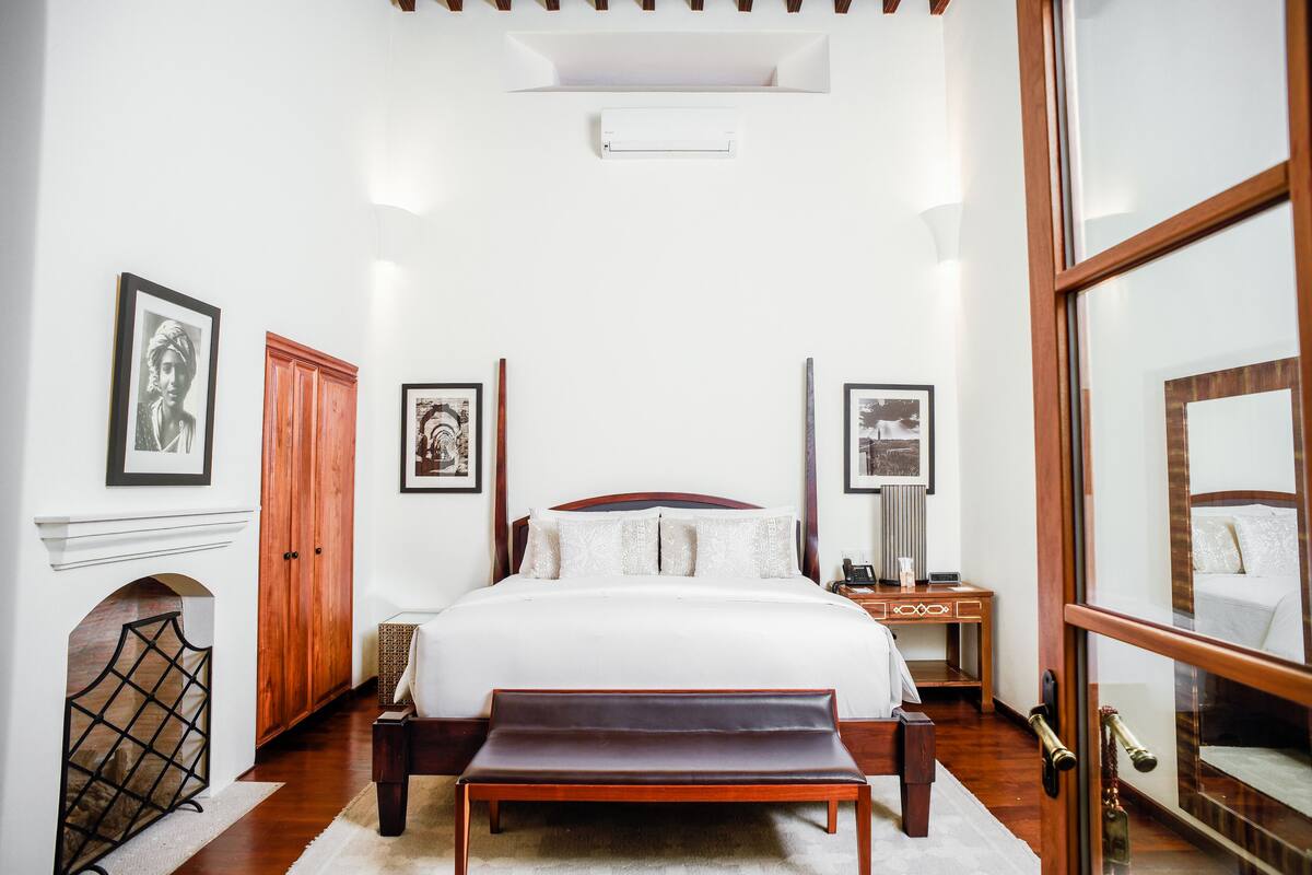 A bedroom with a large bed, a wooden bench, a nightstand, and a mirror.
