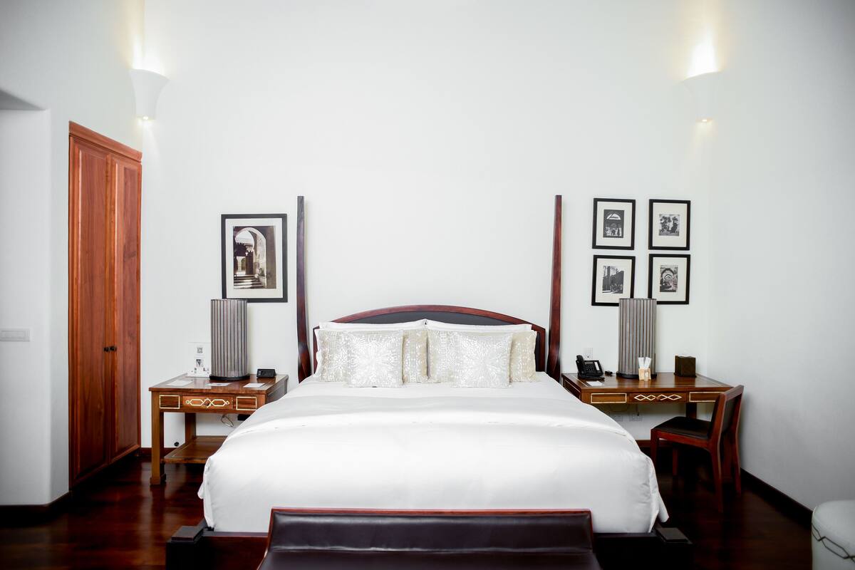 A hotel room with a large bed, wooden wardrobe, bedside tables with lamps, and framed pictures on the walls.