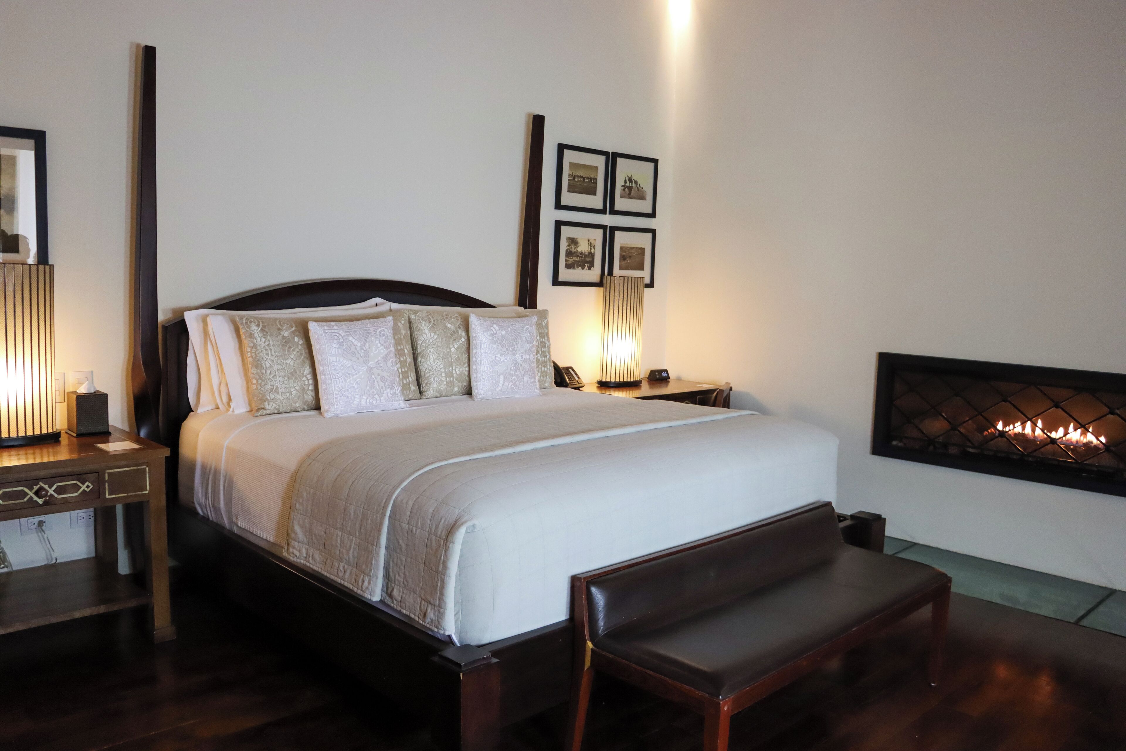 A neatly arranged bedroom with a large bed, bedside tables, a bench, and a fireplace.