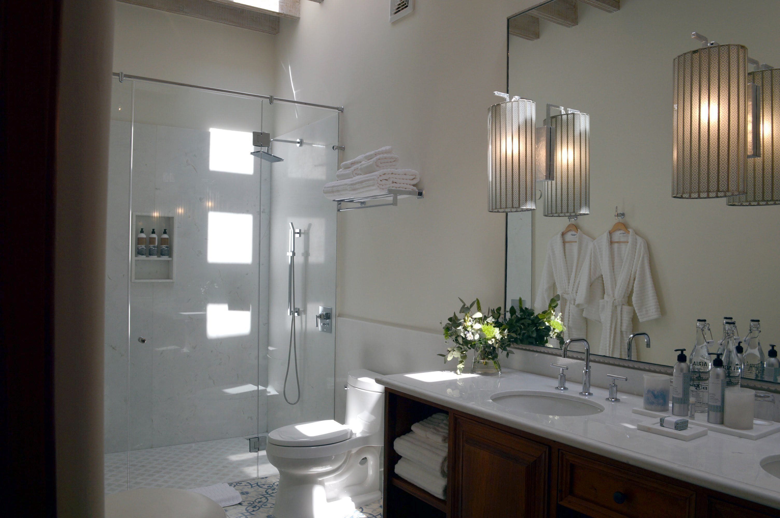 A modern bathroom with a glass-enclosed shower, a white toilet, a vanity with a large mirror, and neatly folded towels.