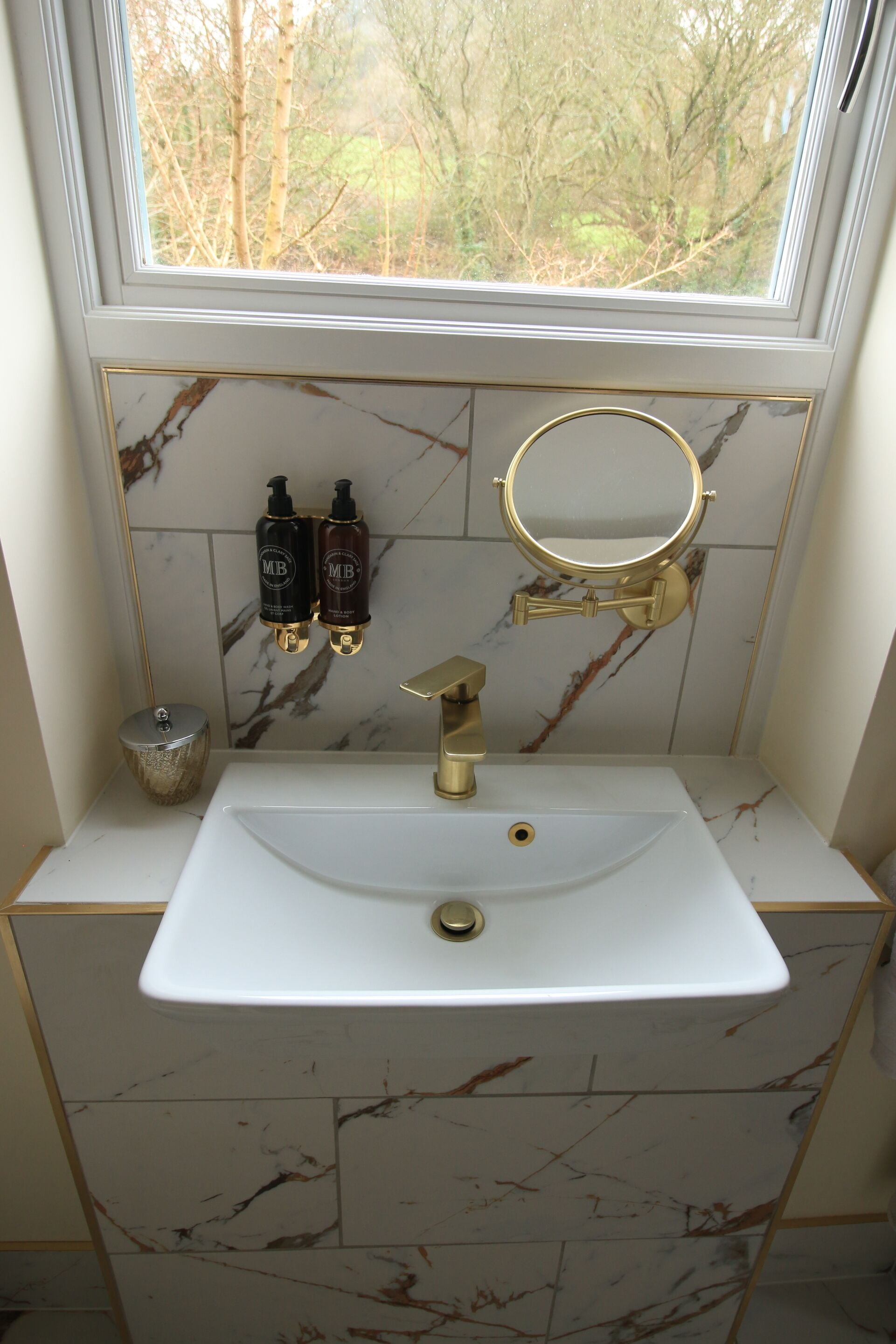 A bathroom with a white sink, gold fixtures, and marble-patterned walls.