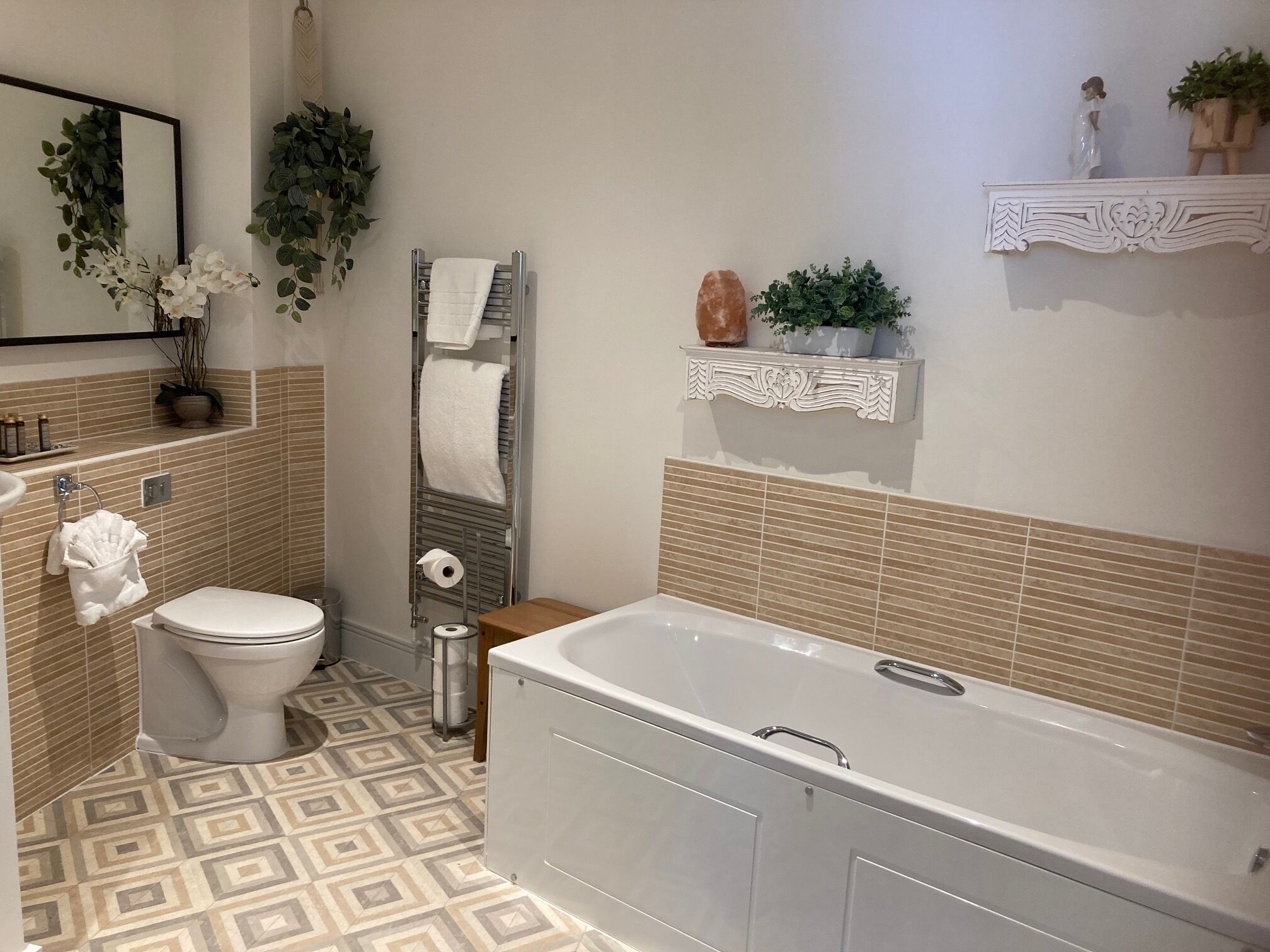 Une salle de bain comprenant des toilettes, une baignoire, un porte-serviettes et une étagère avec des objets décoratifs.