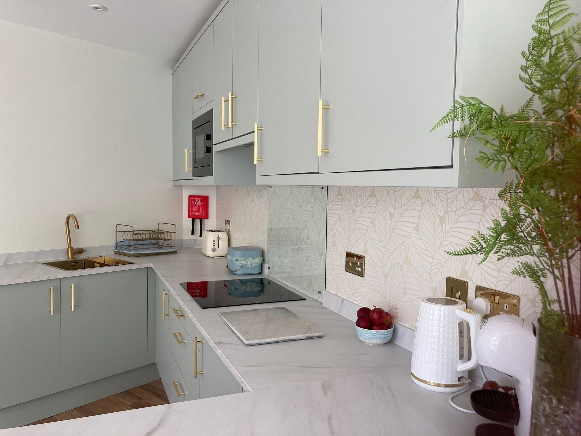 A modern kitchen with grey cabinets, gold handles, a stainless steel sink, a toaster, and a kettle.