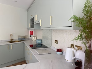 A modern kitchen with grey cabinets, gold handles, a stainless steel sink, a toaster, and a kettle. - Streamside Apartments (Yeovil)