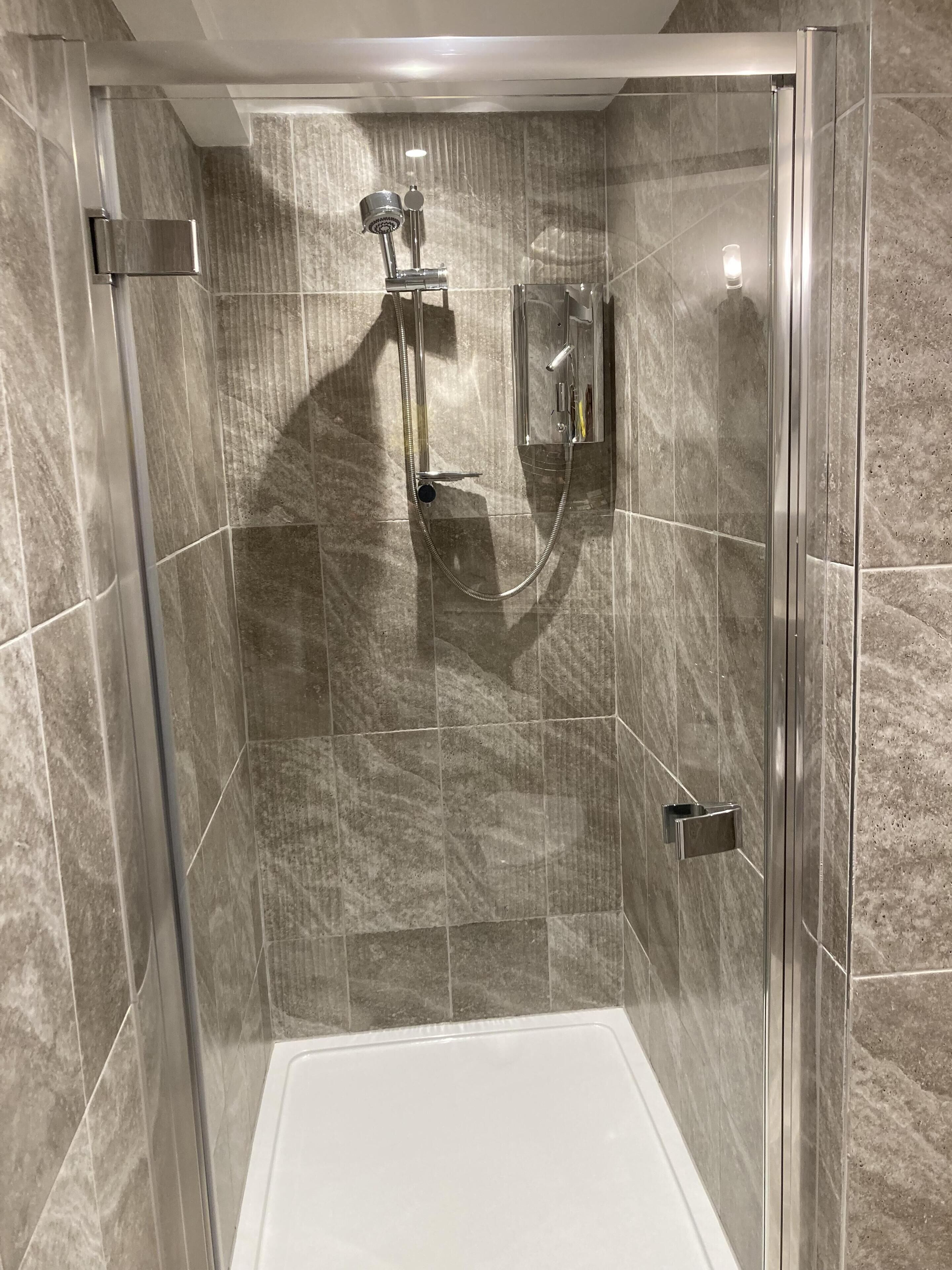 Una cabina doccia in vetro con soffione a mano e rubinetto a parete.