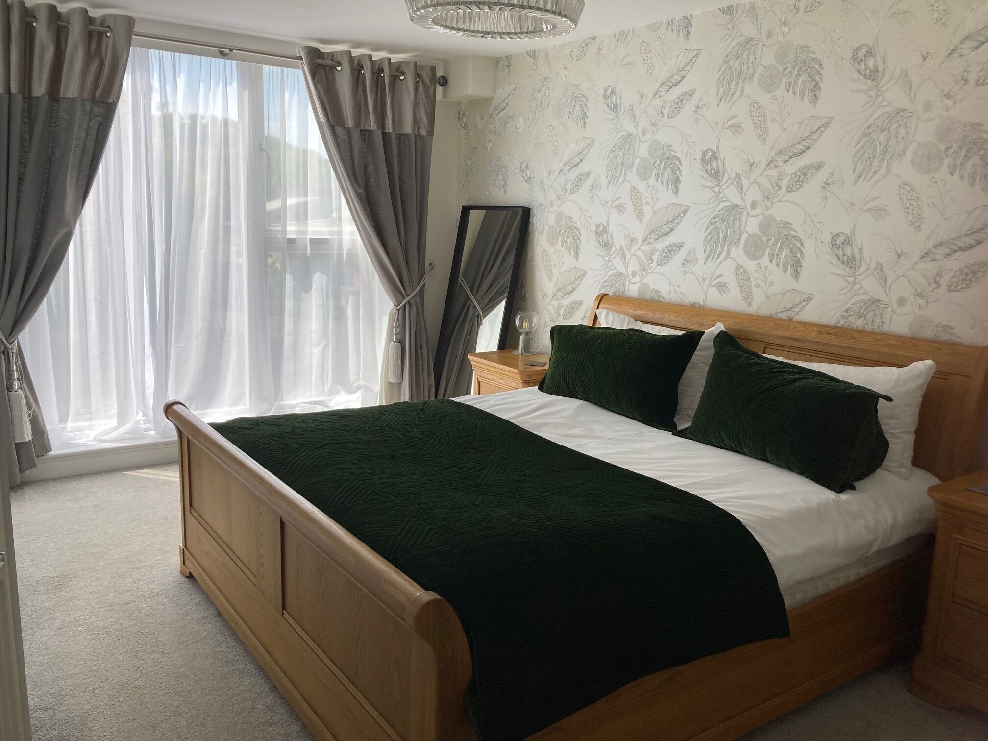 A bedroom with a wooden bed, a nightstand, a mirror, and a window with curtains.