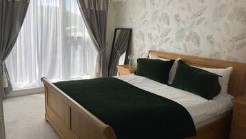 A bedroom with a wooden bed, a nightstand, a mirror, and a window with curtains.
