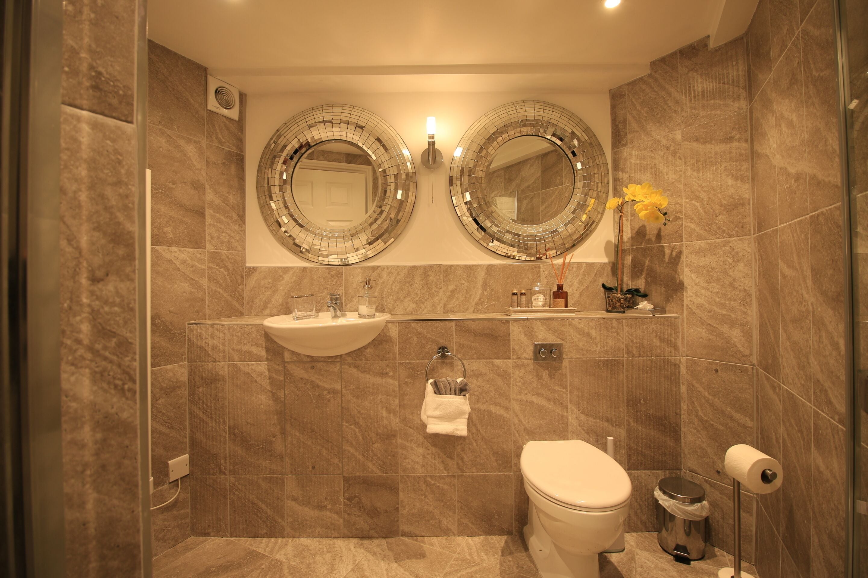 A modern bathroom with two large mirrors, a sink, a toilet, and a shower area.