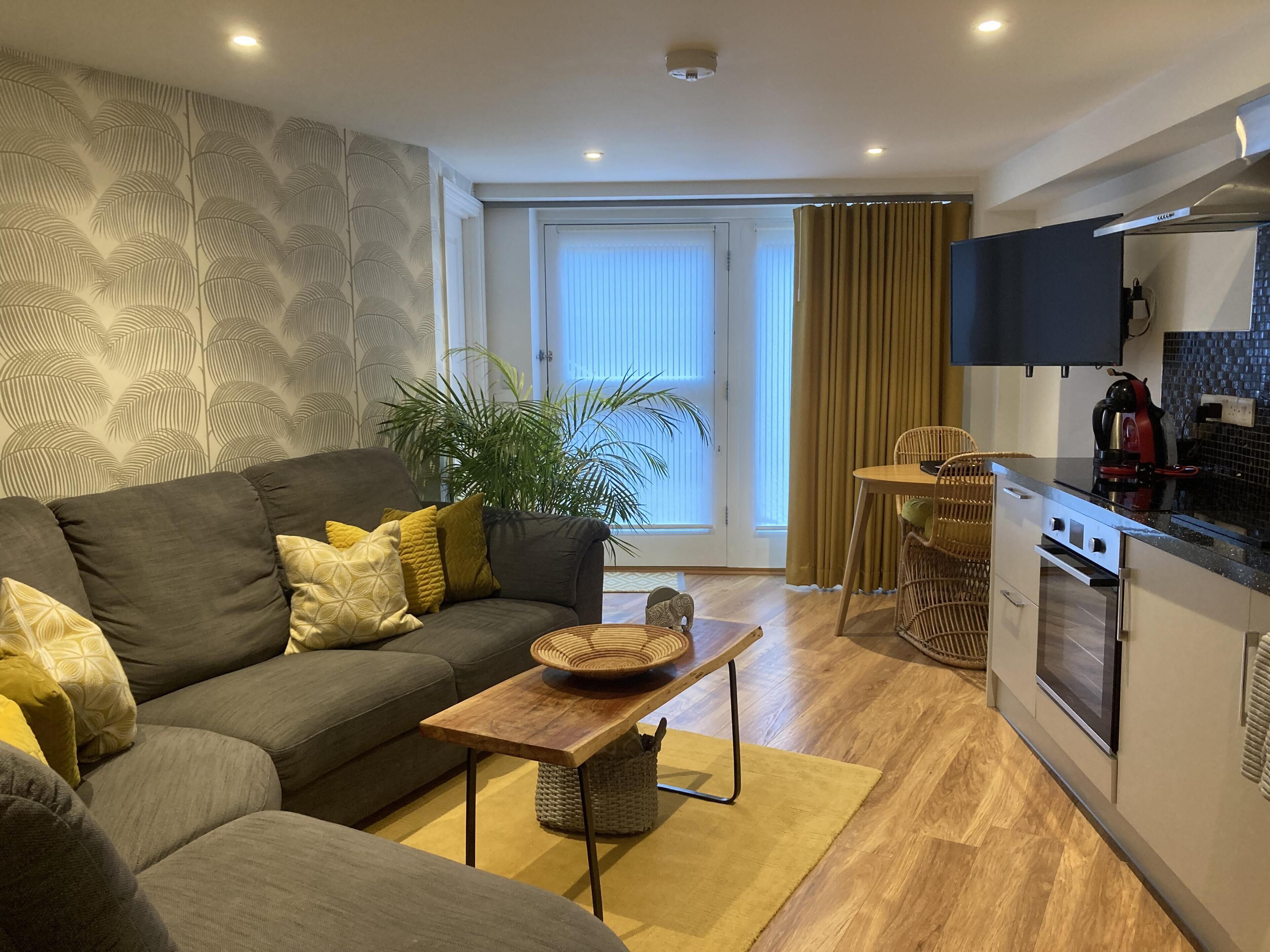 A modern living room with a grey sofa, wooden coffee table, and a large potted plant.