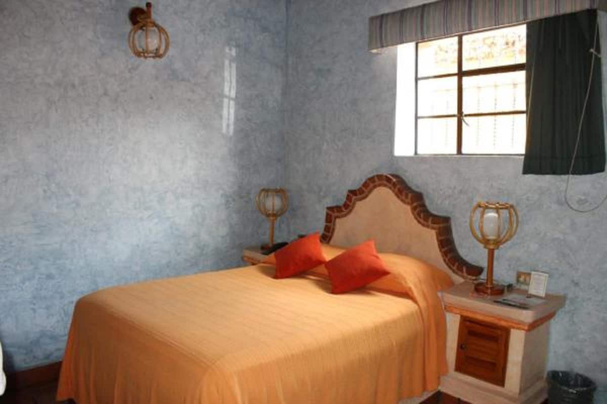 A bedroom with a bed, a nightstand, a lamp, and a window with curtains.