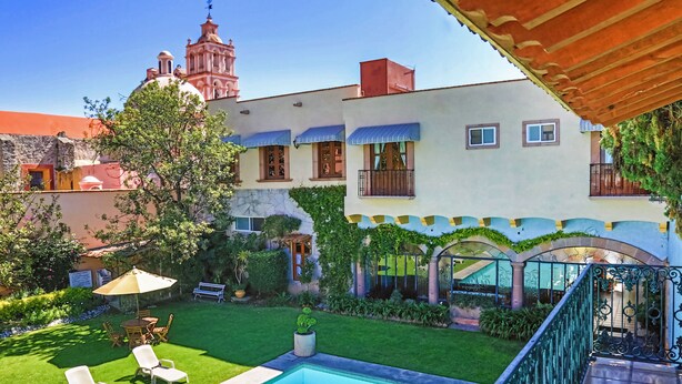 A courtyard with a swimming pool, outdoor seating, and a view of a historic building with a bell tower.