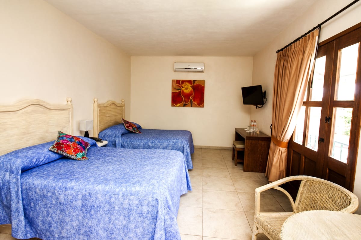 A room with two beds, a television, a window with curtains, and a chair.