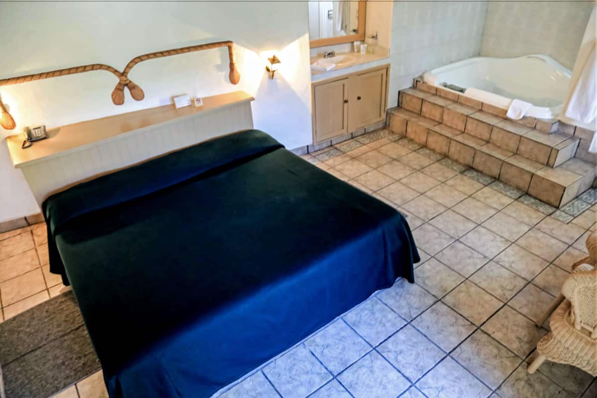 A room with a bed, a bathroom with a bathtub, and a small seating area.